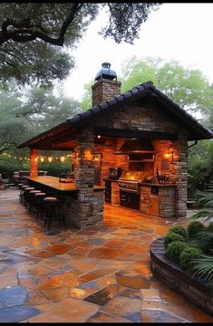 an outdoor kitchen is lit up at night with lights on the grill and bar area