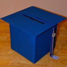 a blue box sitting on top of a wooden floor with a tassel hanging from it's side