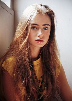 a woman with long hair sitting in front of a window and looking at the camera