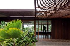 a man standing in the doorway of a house surrounded by greenery and wood panels