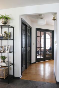 an empty room with black doors and shelves filled with potted plants on top of them