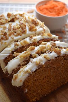 carrot cake with cream cheese frosting and chopped walnuts next to it on a cutting board