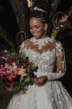 a woman in a wedding dress holds a bouquet and smiles at the camera while standing under a tree