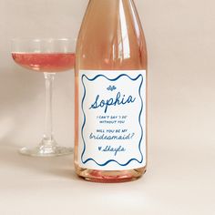 a bottle of wine next to a glass filled with pink liquid on a white surface