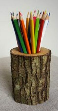 there are many colored pencils in the cup on the tree stump and one is empty