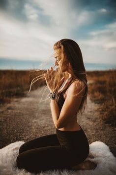 a woman sitting on top of a white rug in the middle of a dirt road