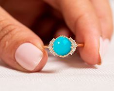 a woman's hand holding a ring with a turquoise stone in the middle and diamonds around it