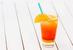 an orange drink with a blue straw in a glass on a white wooden table top