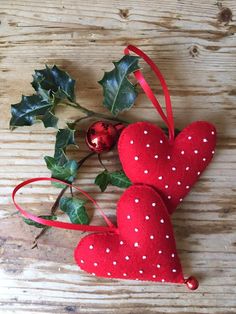 two red hearts with white polka dots on them and holly leaves hanging from the stems