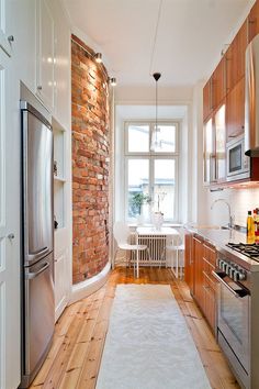 a narrow kitchen with brick wall and wooden flooring, along with stainless steel appliances