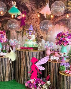 a table topped with lots of cake next to flowers and fairy figurines on top of wooden stumps