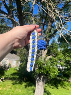 a hand holding a blue and white crocheted object in front of a tree