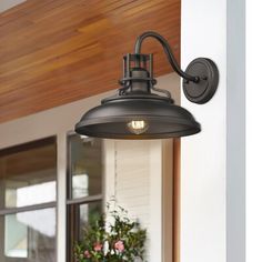 an outdoor light hanging from the side of a house next to a potted plant