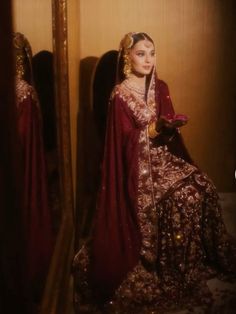 a woman in a red and gold dress looking at herself in the mirror