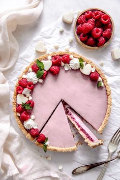 a pie with raspberries and white flowers on it next to a bowl of strawberries