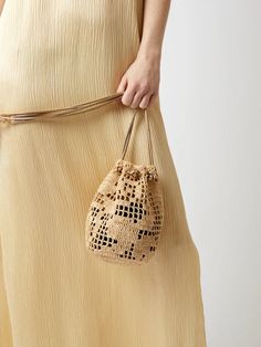 a woman in a beige dress is holding a bag that has holes on the side