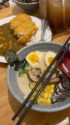 two chopsticks resting on a bowl of food with rice and other foods in the background