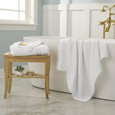 a white bath tub sitting in a bathroom next to a wooden stand with towels on it