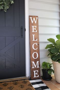 a welcome sign sitting next to a door with potted plants on the front porch