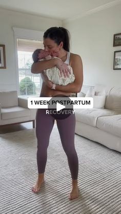 a woman holding a baby in her arms while standing on a carpeted living room floor