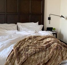 the bed is made up with white linens and brown fur on it's headboard