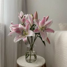 a vase with pink flowers sitting on a small table next to a white curtained window