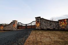 a stone gate with christmas decorations on it and a driveway leading up to the entrance