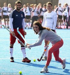 two women playing field hockey on an outdoor court with people watching from the sidelines