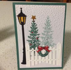 a card with a christmas tree and a lamp post on the table next to it