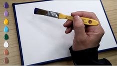 a person holding a paintbrush over a piece of paper with water drops on it