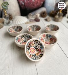 six small bowls with designs on them sitting on a table next to shells and seashells