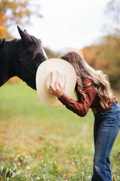 a woman is kissing a horse's nose with a hat on her head in the grass