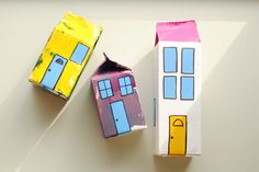 two cardboard houses sitting next to each other on top of a white table with one painted yellow and the other pink