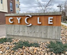 a sign that says cycle apartments in front of some rocks and bushes on the sidewalk