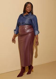 a woman standing in front of a wall wearing a blue shirt and purple leather skirt