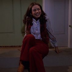 a young woman sitting on the steps in front of a door wearing red pants and a white shirt