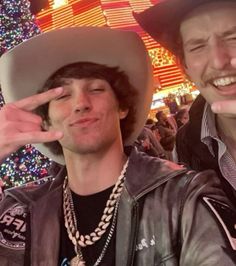 two men in cowboy hats standing next to each other at a christmas tree event with lights on the trees behind them