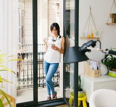 a woman standing in front of a door looking at her cell phone while holding a coffee cup