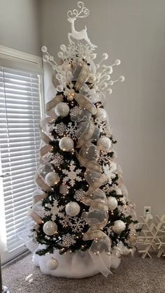 a decorated christmas tree with white and silver ornaments on it's base, in front of a window