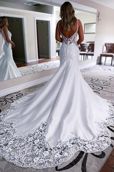 a woman in a white wedding dress looking at herself in the mirror with her back to the camera