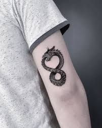 a man's arm with a black and white dragon tattoo on the left forearm