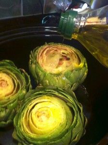 three artichokes in a pan with oil being poured on them