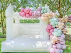 an inflatable arch is decorated with balloons and pastel colors on the grass