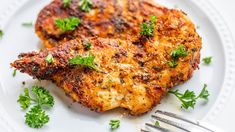 two pieces of chicken on a white plate with parsley garnish and a fork