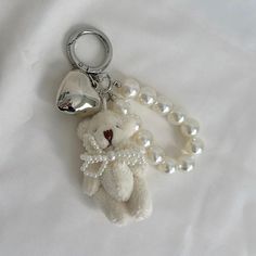 a white teddy bear with pearls and a heart shaped keychain on a white sheet