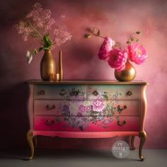 two vases with flowers sit on top of a chest of drawers in front of a pink wall