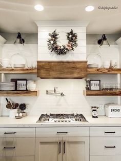 a white kitchen with open shelves and wreath on the wall above the stove top,