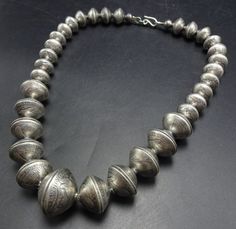 BUFFALO DANCER (TAOS) GRADUATED COIN BEAD NECKLACE DESCRIPTION:  This impressive necklace is made from old 90% silver coins beginning with Mercury dimes, intensifying to Standing Liberty quarters, with a center bead made from a pair of Walking Liberty half dollars. This outstanding necklace will be a valuable addition to your collection of fine Native American jewelry. MEASUREMENTS:  Necklace measures 21" end to end Center bead measures 25mm across Beads are securely strung on silver foxtail cha Vintage Wedding Necklaces With Silver Beads, Vintage Necklaces With Sterling Silver Clasp, Vintage Silver Necklaces With Round Beads, Antique Silver Stamped Necklaces, Vintage Silver Round Bead Necklaces, Antique Silver Stamped Necklace, Classic Etched Necklace For Collectors, Vintage Silver Beaded Necklaces, Vintage Silver Necklaces With Polished Beads