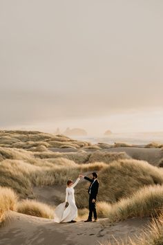 a bride and groom walking through the sand dunes