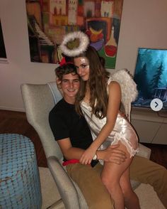 a young man and woman sitting on a chair in front of a television screen with an angel costume over their heads